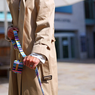Colour Stripe organic cotton multipurpose lead and waste bag holder held together, with a beige trench coat and civic square background